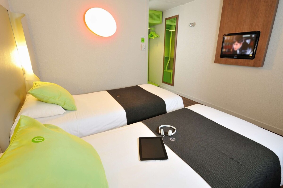 A hotel room with two beds, a bedside table, a TV, and a mirror.