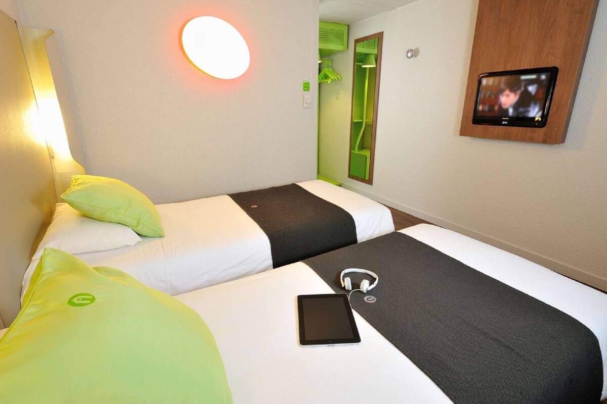 Ein Hotelzimmer mit zwei Betten, einem Nachttisch, einem Fernseher und einem Spiegel.