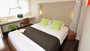 Habitación de hotel con cama, escritorio con una computadora portátil, silla y mesita de noche con lámpara.