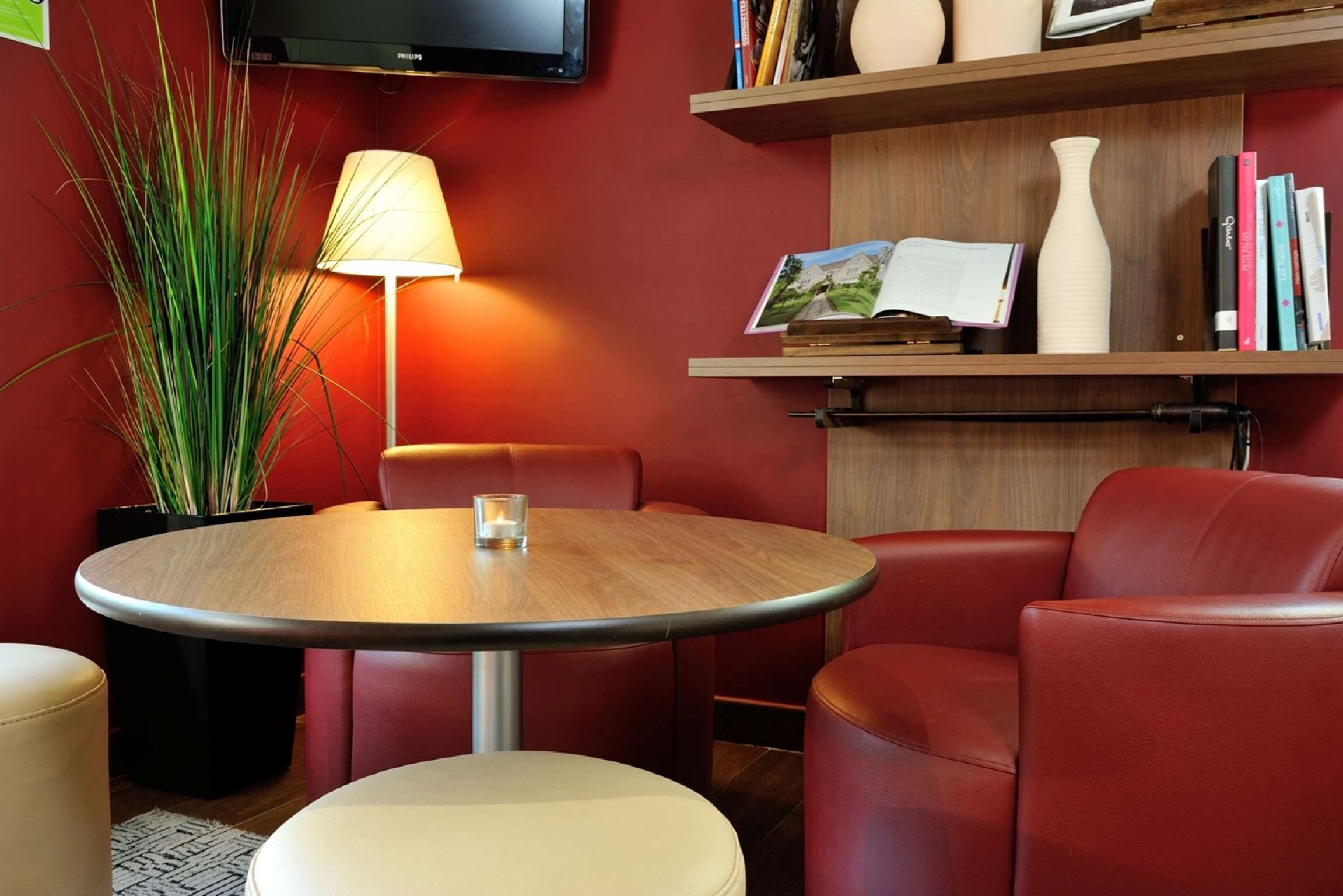 Une pièce moderne avec une table ronde en bois, des fauteuils en cuir rouge, un lampadaire, une plante en pot et une étagère contenant des livres et des objets décoratifs.