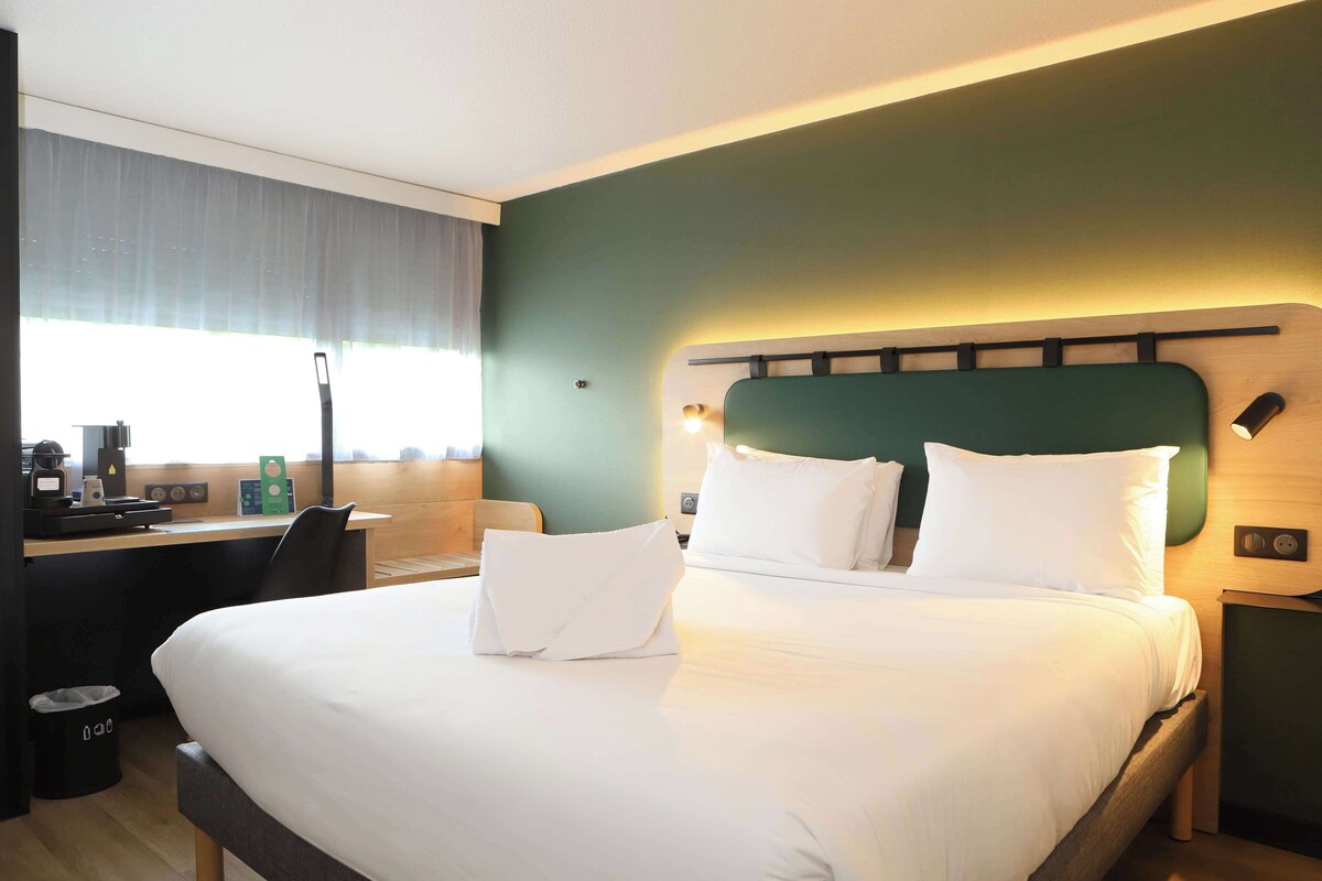 Une chambre d’hôtel avec un grand lit, un bureau avec un ordinateur et une fenêtre avec des rideaux.