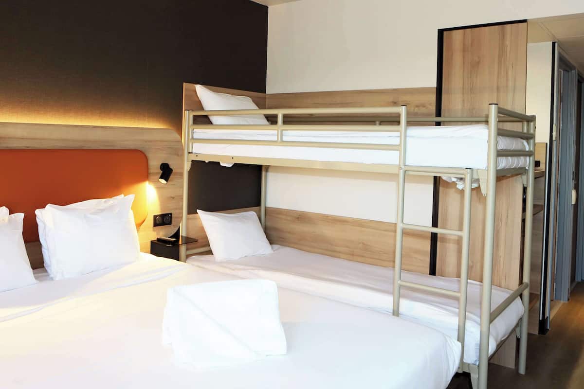 A bunk bed room with a wooden headboard, white bedding, and a nightstand with a lamp.