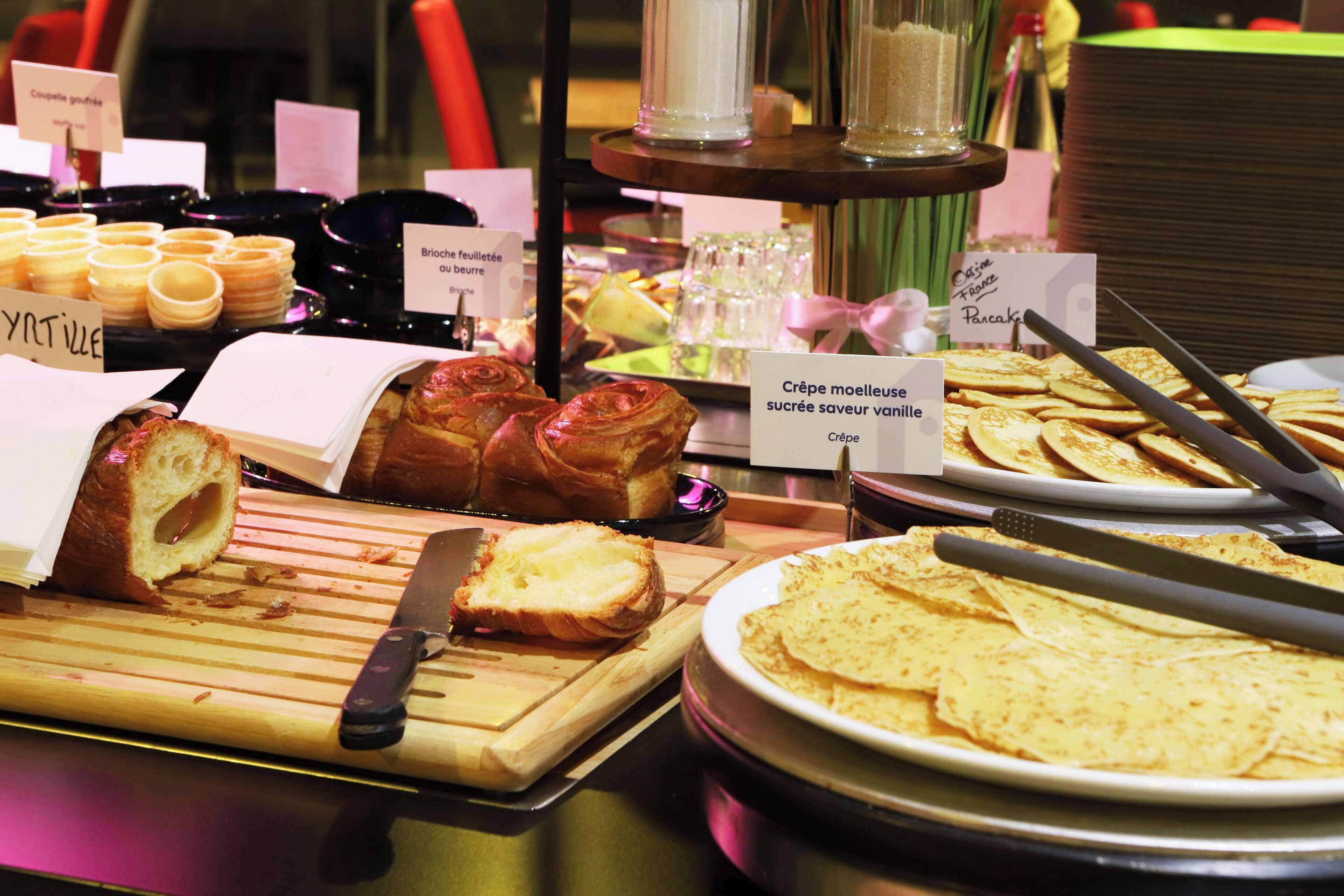 A buffet with various food items including pastries, a cutting board with a knife, and a plate of crepes.