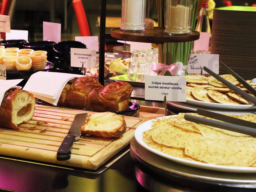 A buffet with various food items including pastries, a cutting board with a knife, and a plate of crepes.