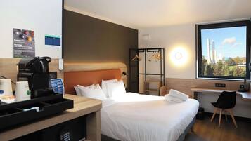 A hotel room with a bed, a desk, a coffee machine, and a window with a view of a rocket launch.