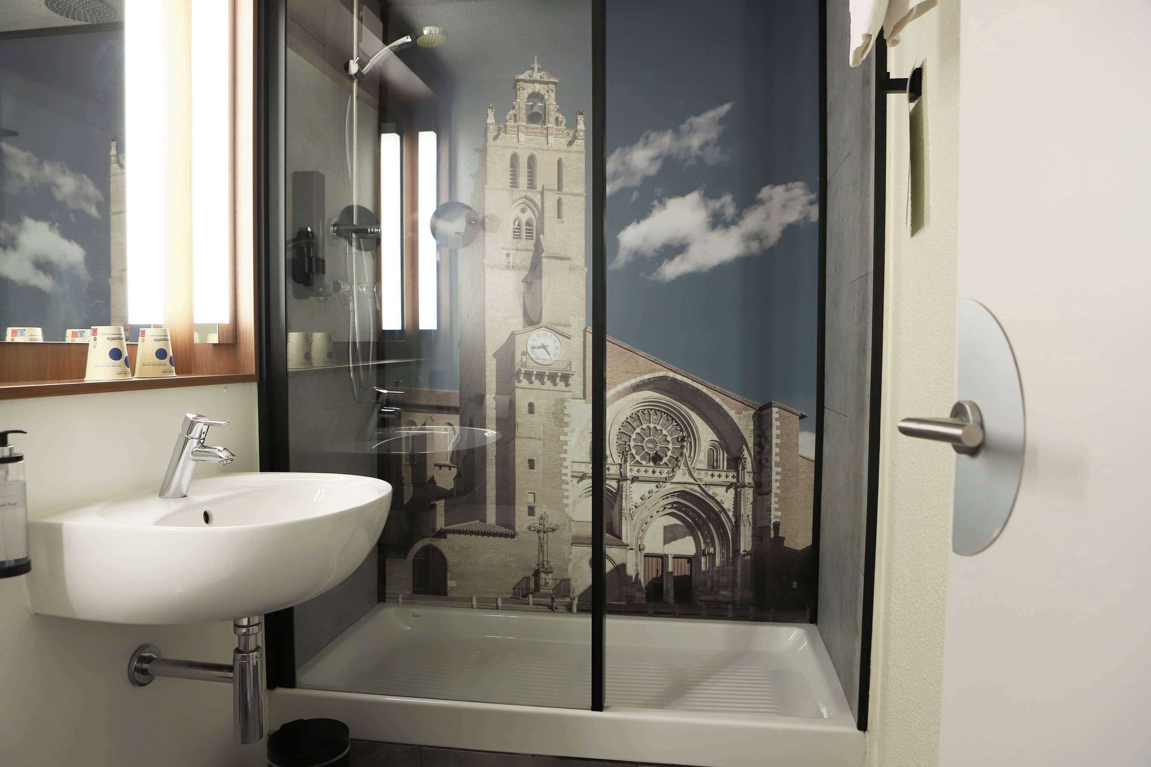 A bathroom with a white sink, a glass-enclosed shower, and a mural of a cathedral.