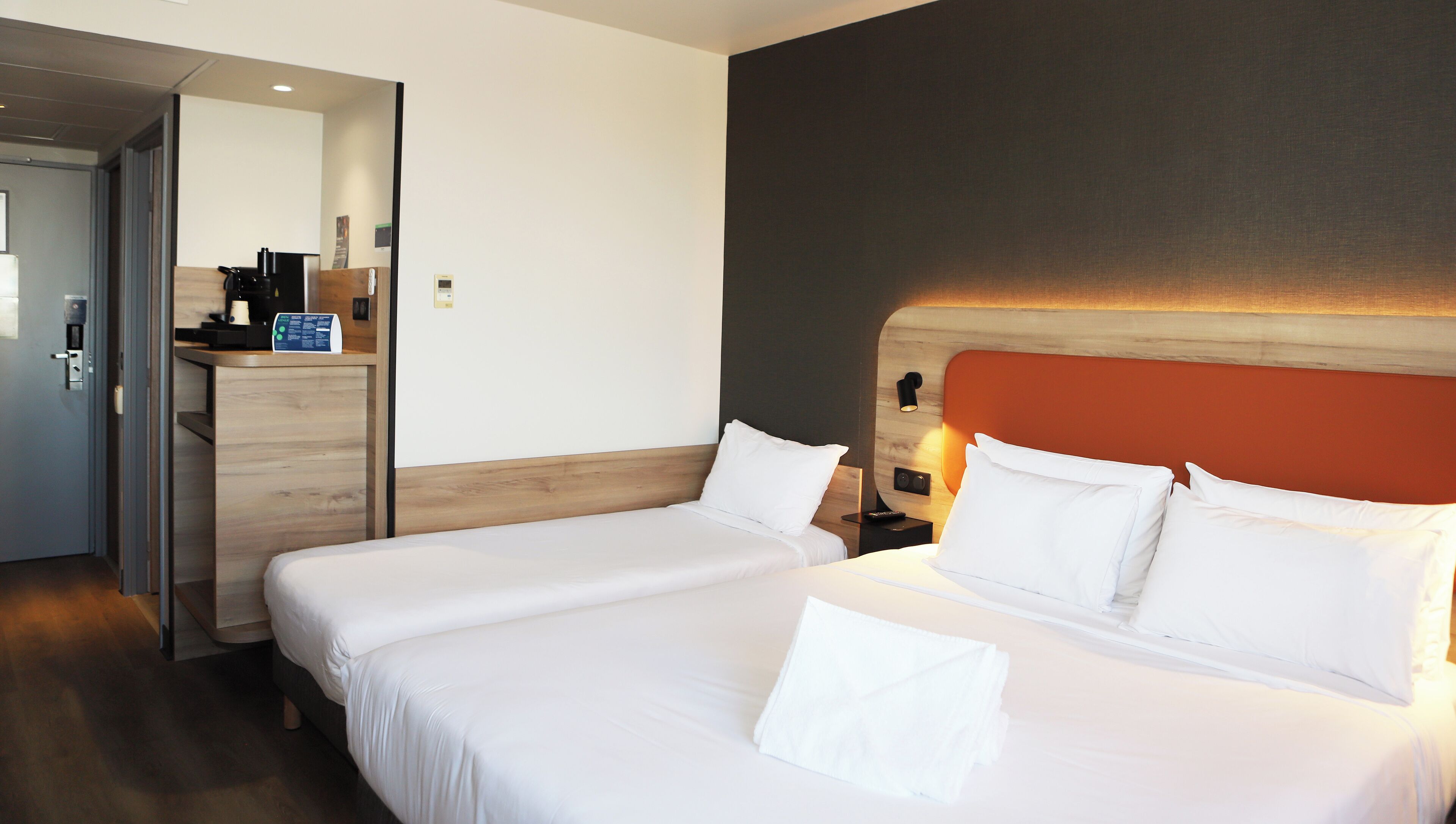 A hotel room with two beds, a desk with a coffee machine, and a mirror.