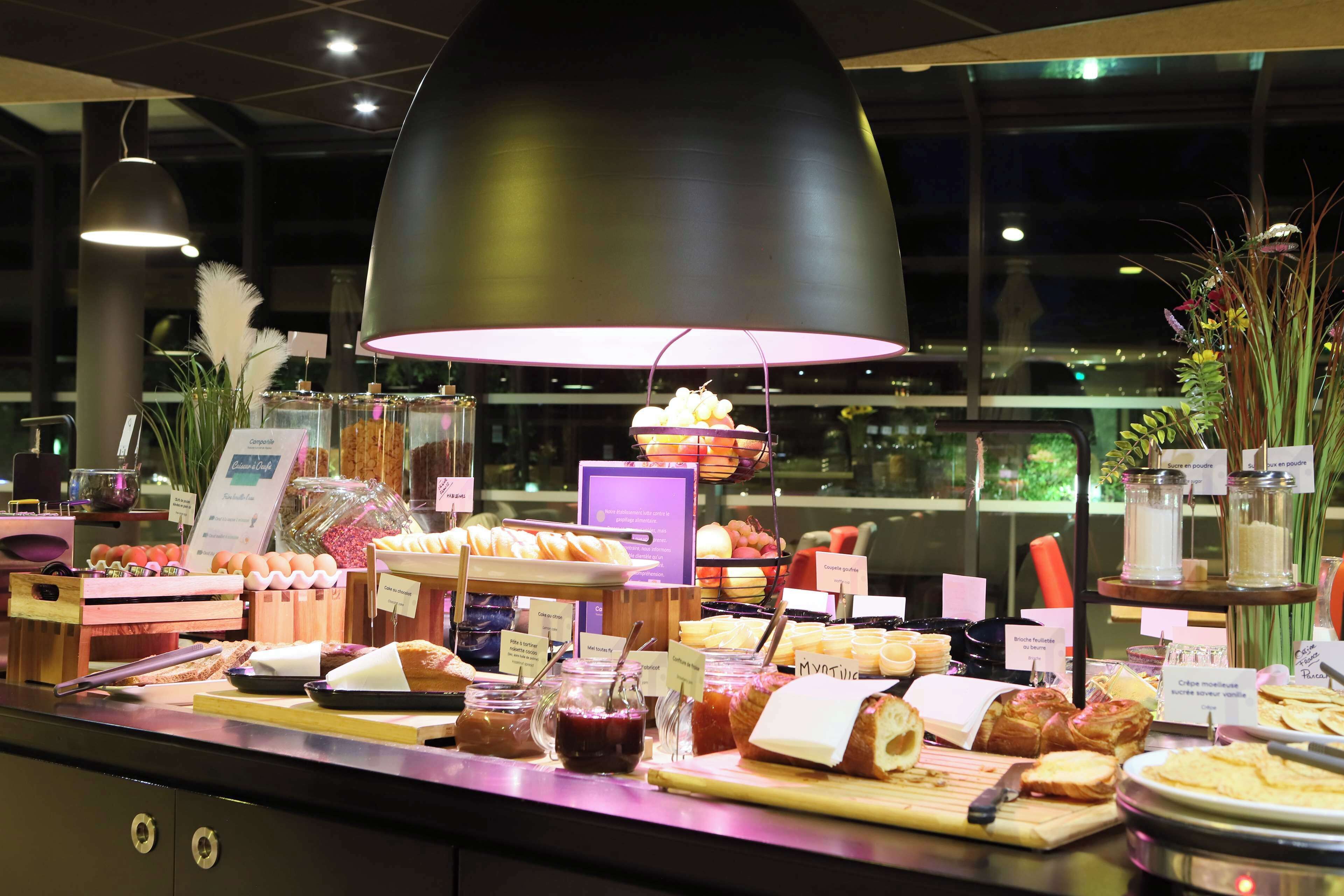 A buffet with various food items and a large black pendant light above.
