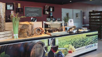 A café counter with a menu board, wine glasses, and a large poster advertising 'Campanile'.