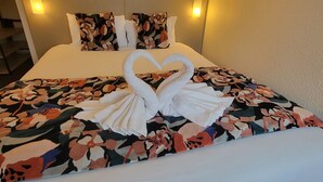 Habitación de hotel con una cama, un edredón con motivos florales y una confección de toallas en forma de dos cisnes.