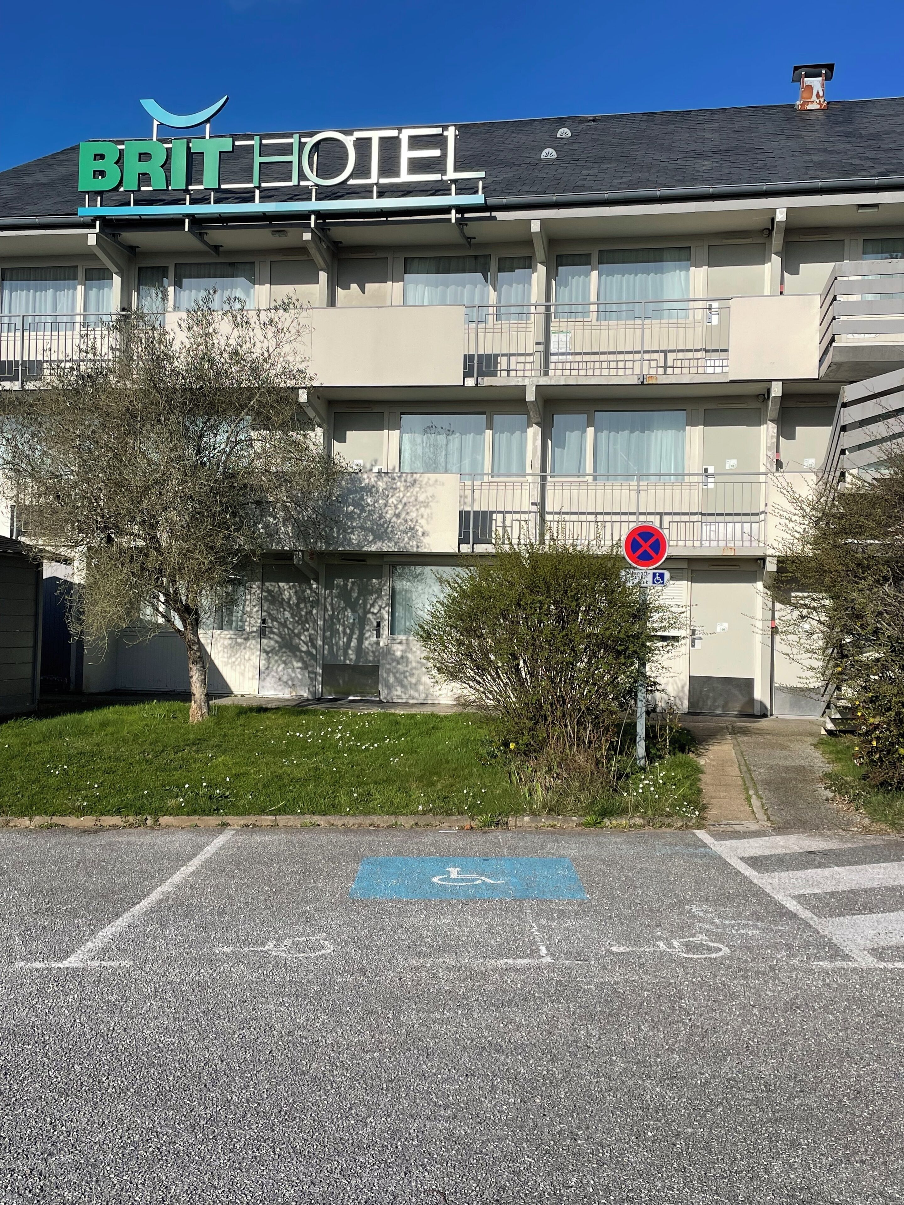 Un hotel llamado BRITHOTEL con un letrero en el techo, un cartel de ‘prohibido estacionar’ y un espacio reservado para discapacitados.
