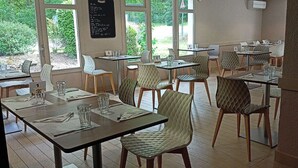 Un restaurante con varias mesas y sillas, amplios ventanales con vistas a zonas verdes y un menú en una pizarra en la pared.