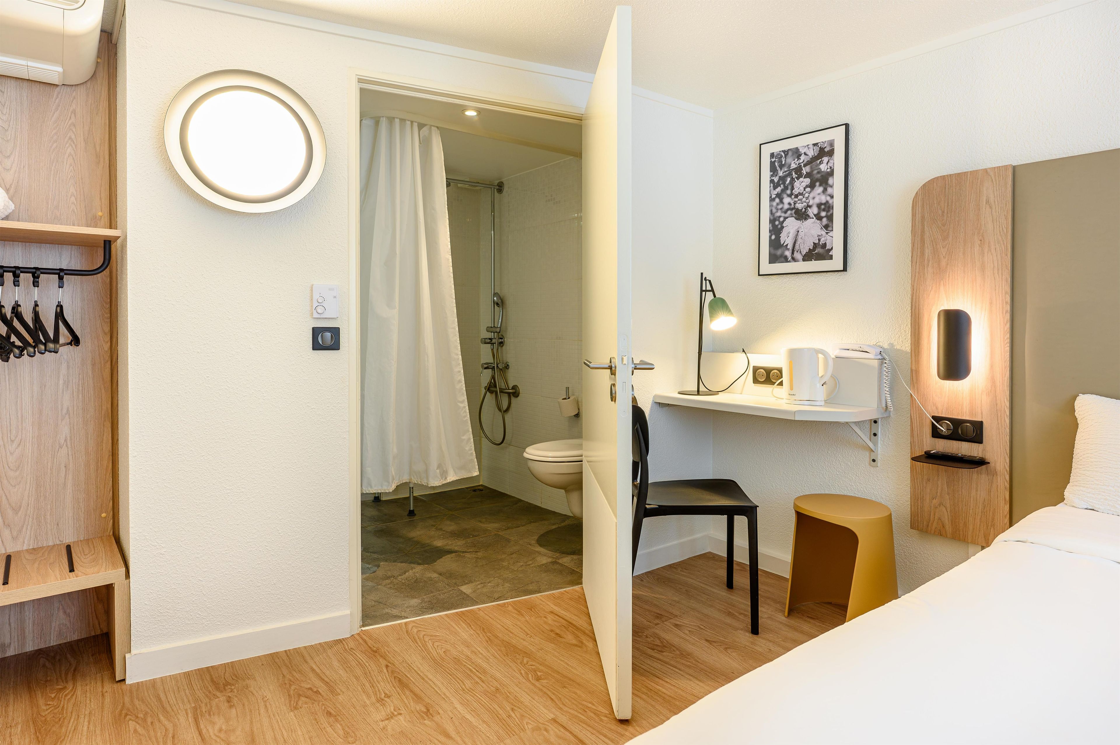 Een hotelkamer met douche, toilet, nachtkastje, stoel en een bed.