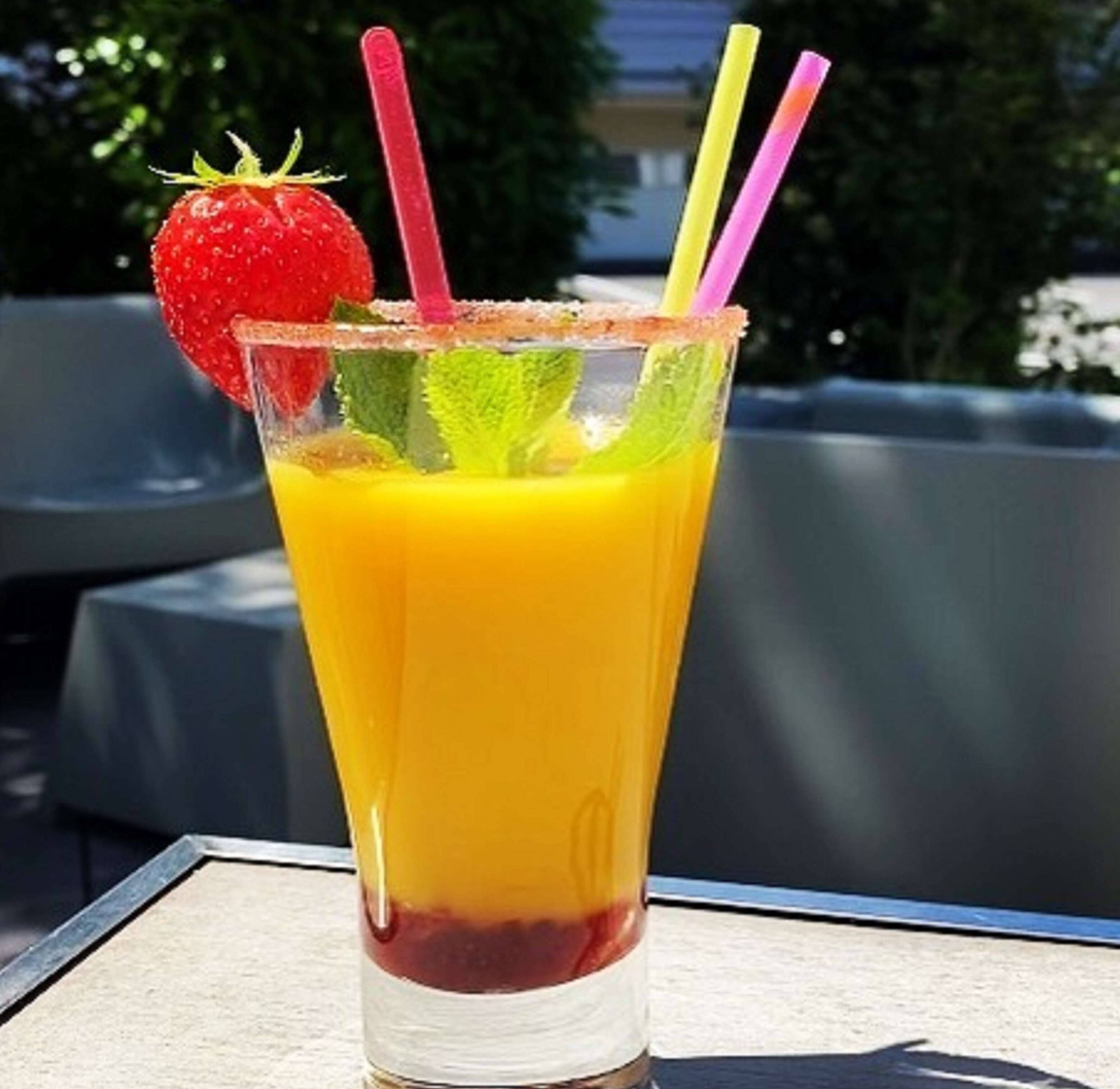 A glass of orange juice with a strawberry garnish and two straws.