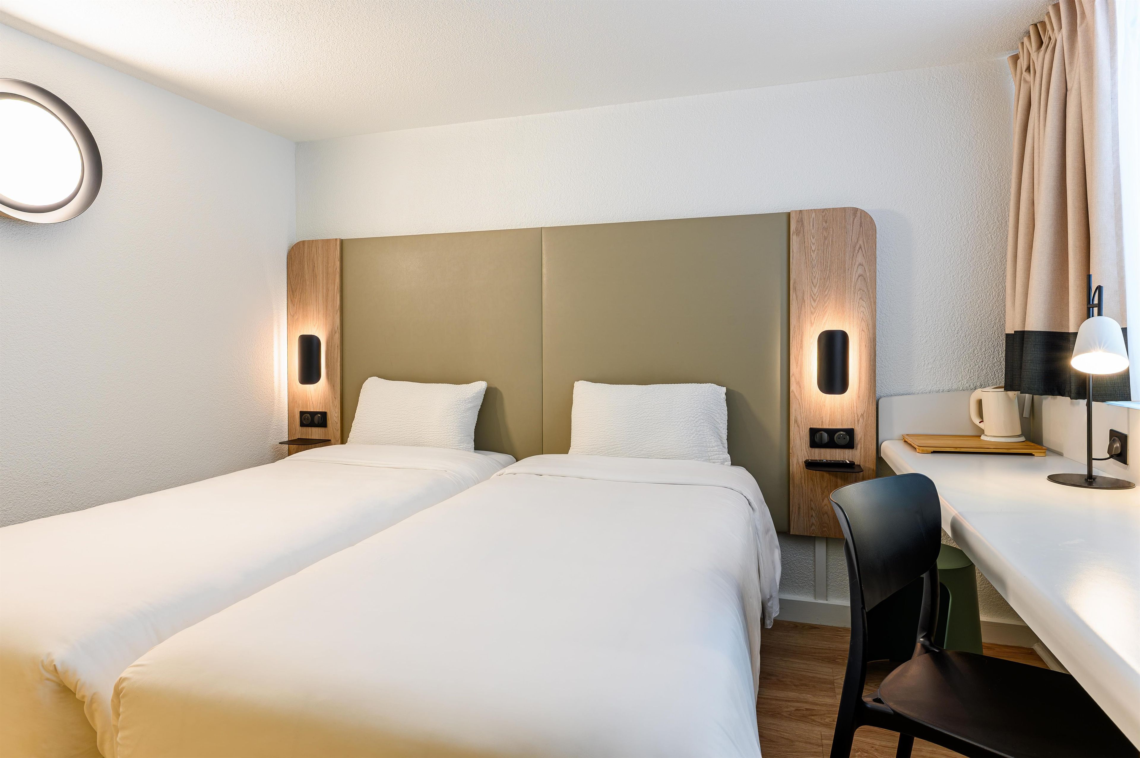 Une chambre d’hôtel avec deux lits, un bureau, une chaise et une machine à café.