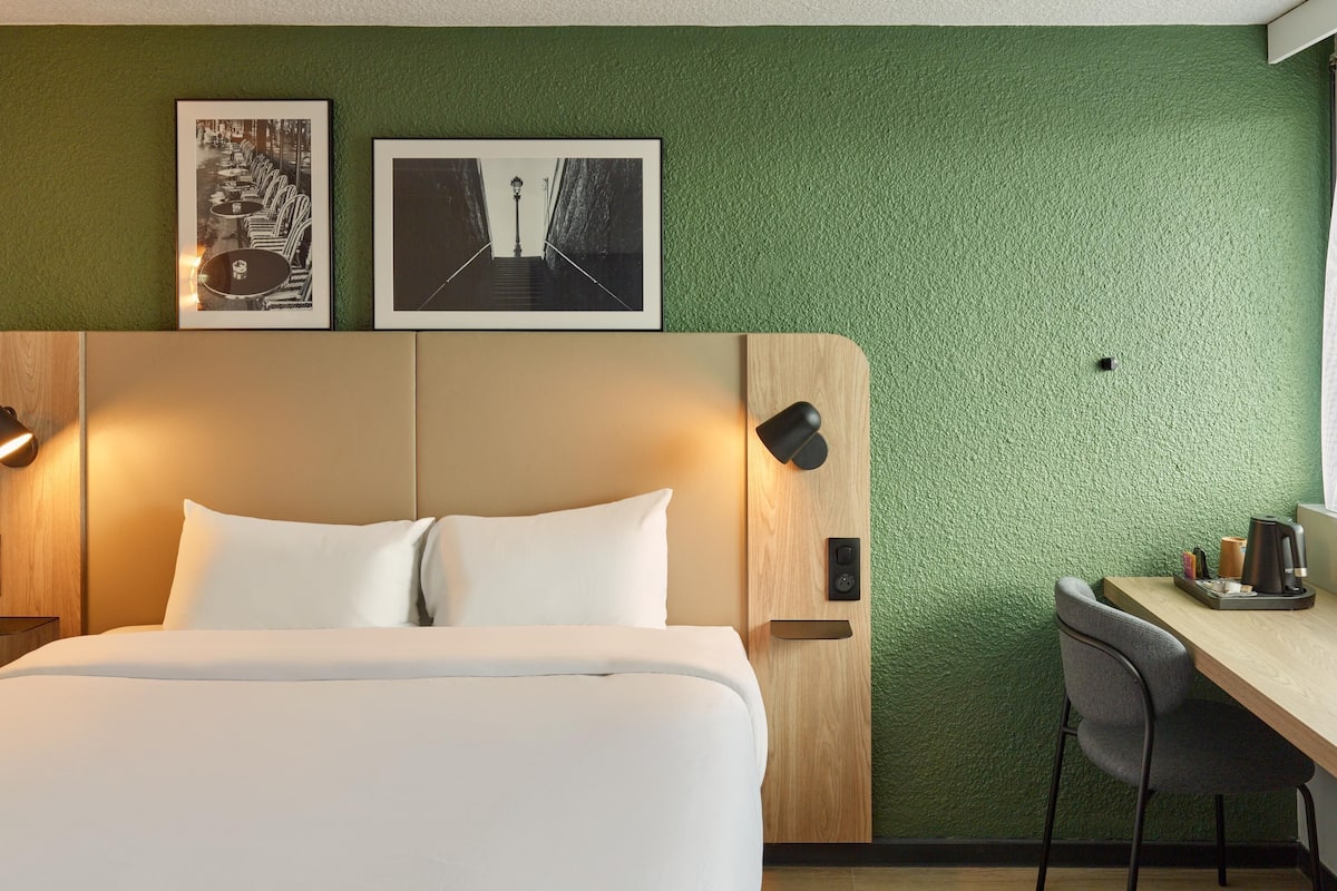 A hotel room with a bed, a desk, and two framed pictures on the wall.