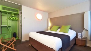 A hotel room with a bed, a green wall unit, a wooden chair, and a nightstand with a lamp. - Campanile NATURE - Tours Sud Joué lès Tours le Lac (Joue-les-Tours)