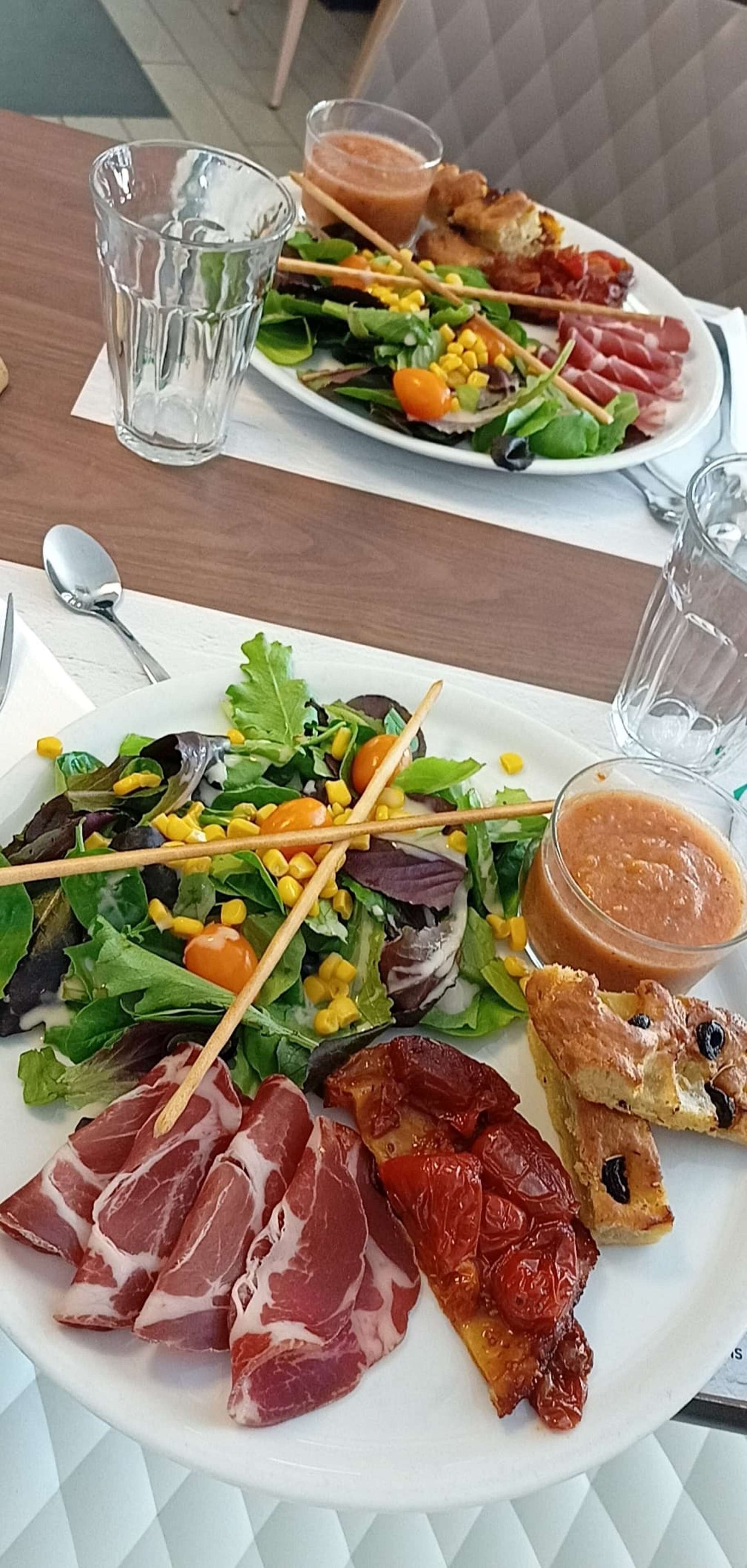 Ett matbord med två tallrikar mat, inklusive sallader och kött, och två glas vatten.