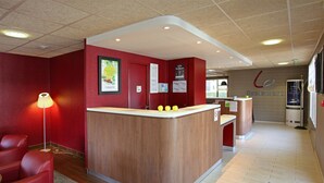 Interior de restaurante con mostrador de madera, paredes rojas y una mesa de recepción.