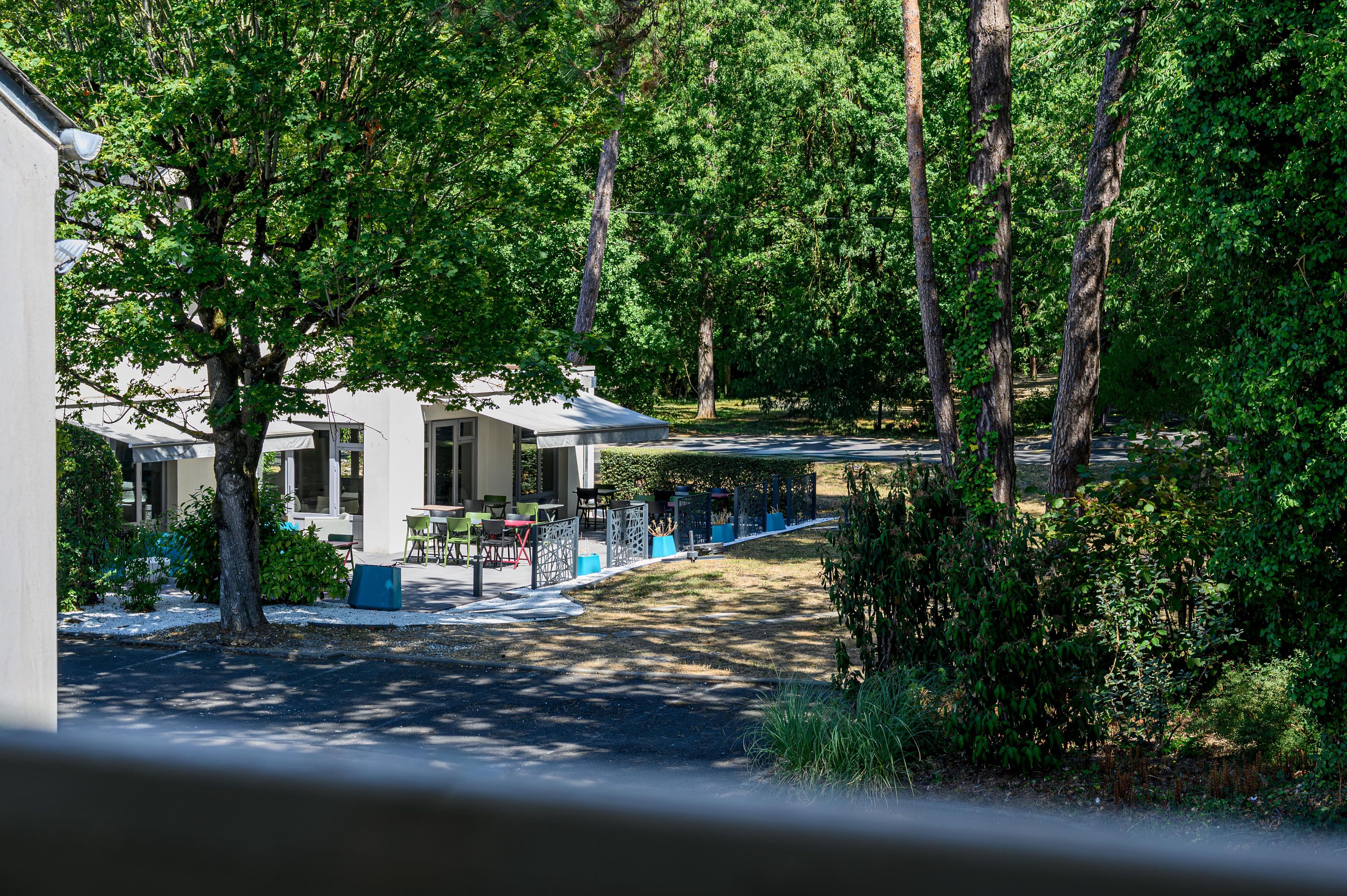 A row of single-story buildings with outdoor seating areas, surrounded by dense greenery.