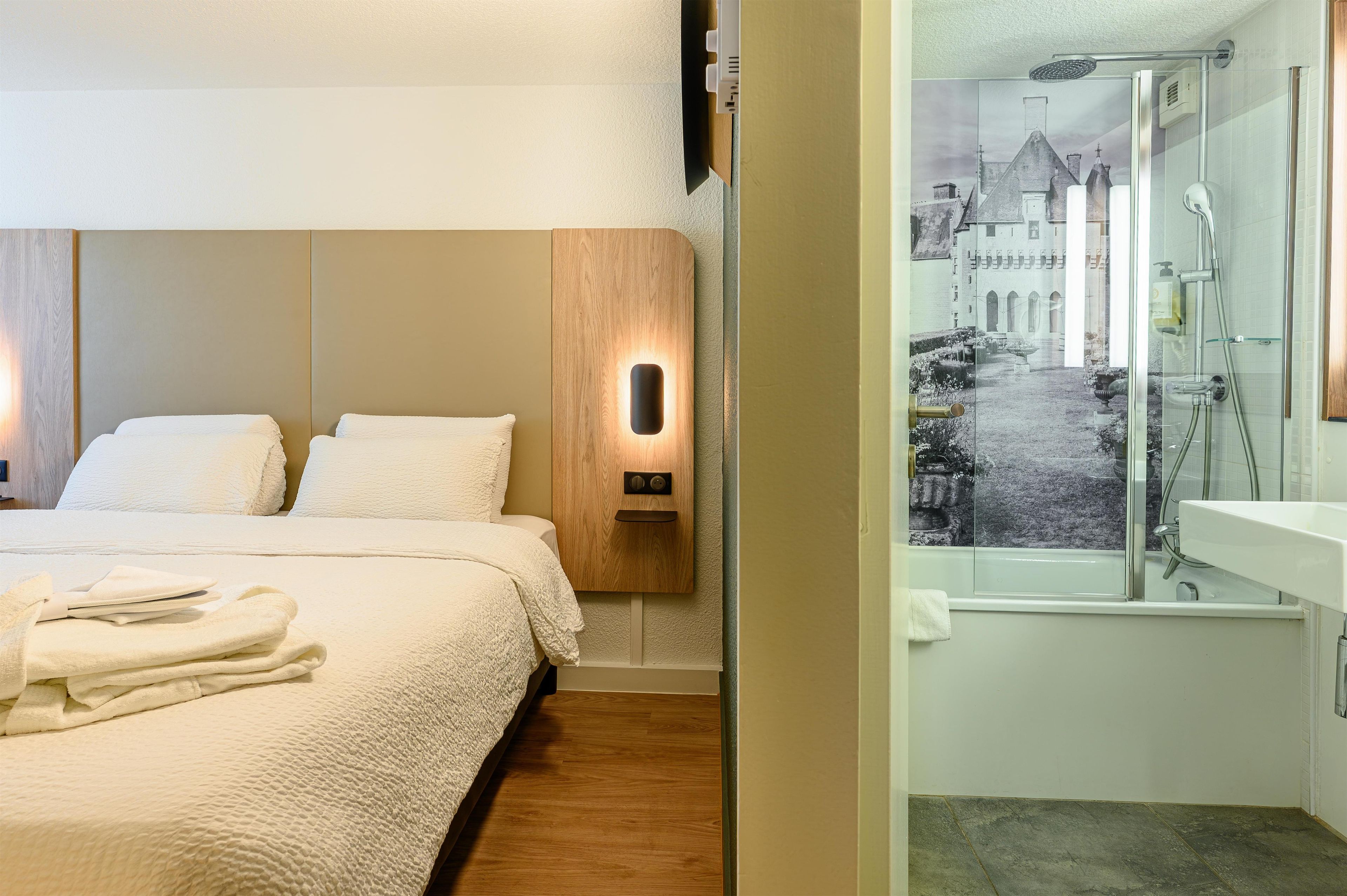 Habitación de hotel con cama, cabecero de madera, luz empotrada en la pared y vista a un edificio histórico a través de una puerta de cristal.