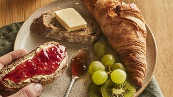A plate with a croissant, a slice of bread with jam, grapes, kiwi slices, and a spoon.