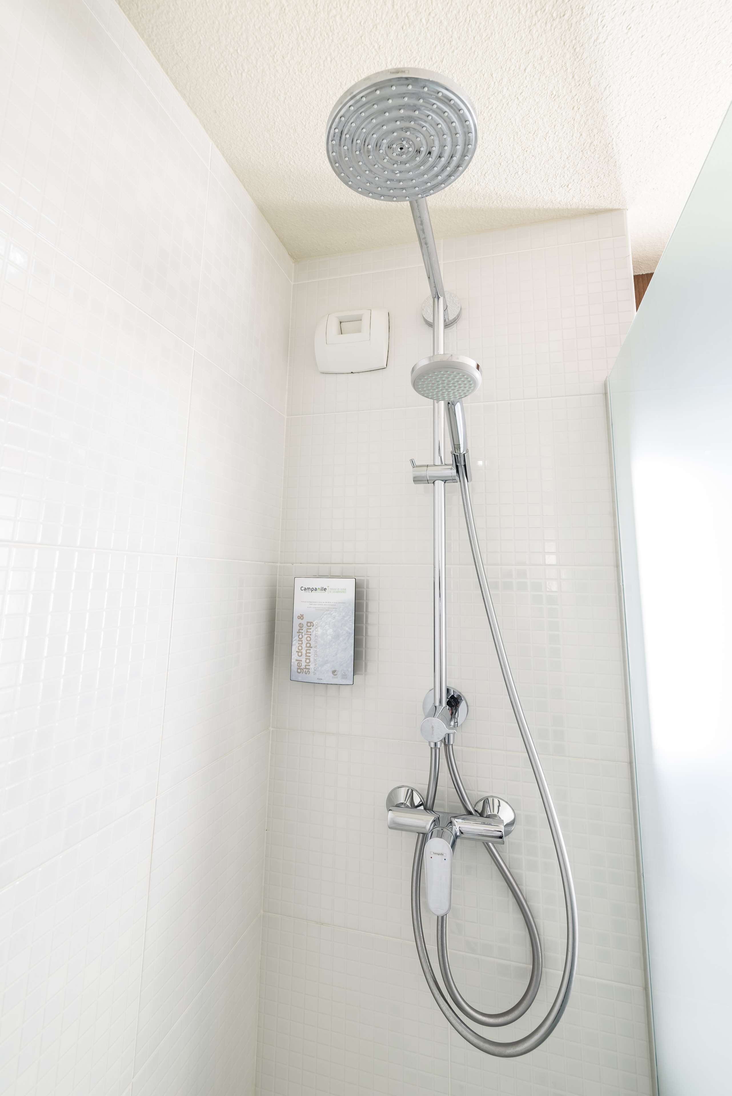 Una ducha con cabezal de ducha manual y panel de control en la pared.