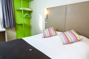 A hotel room with a bed, two patterned pillows, a green wardrobe, and a wall-mounted light. - Campanile Toulouse Ouest - Purpan (Toulouse)