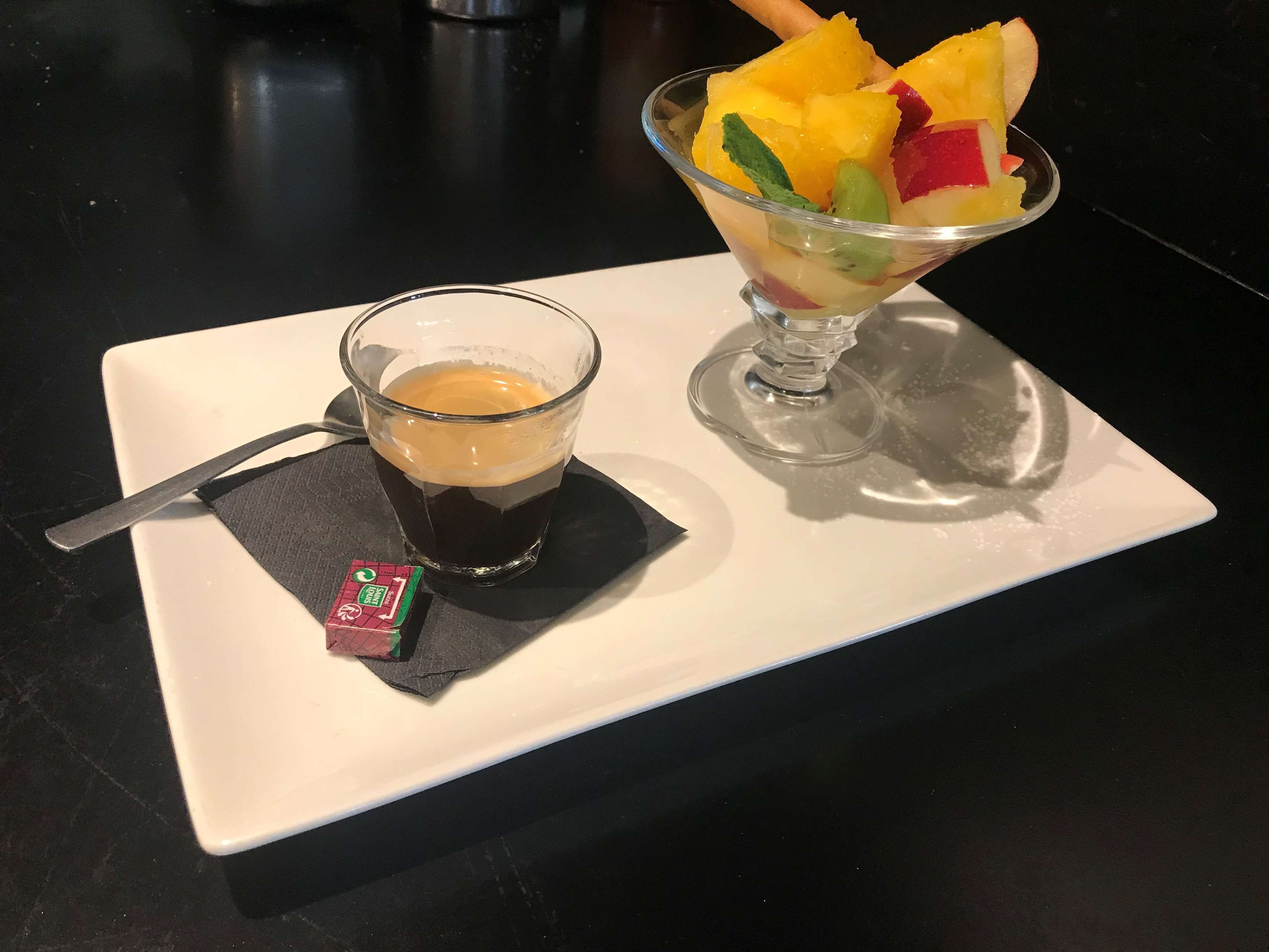 Un postre con fruta y un vaso de líquido oscuro, posiblemente café, sobre un plato blanco.