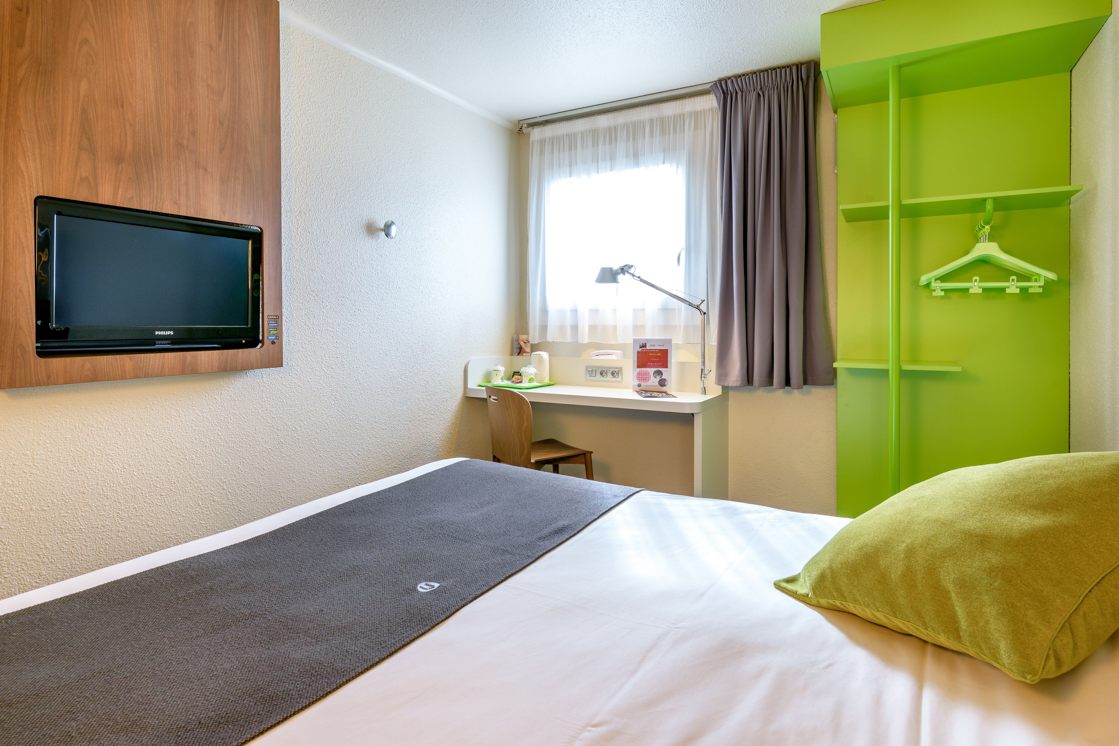 Une chambre d’hôtel avec un lit, un bureau doté d’une lampe, une télévision et une armoire verte.