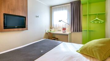 Une chambre d’hôtel avec un lit, un bureau doté d’une lampe, une télévision et une armoire verte.