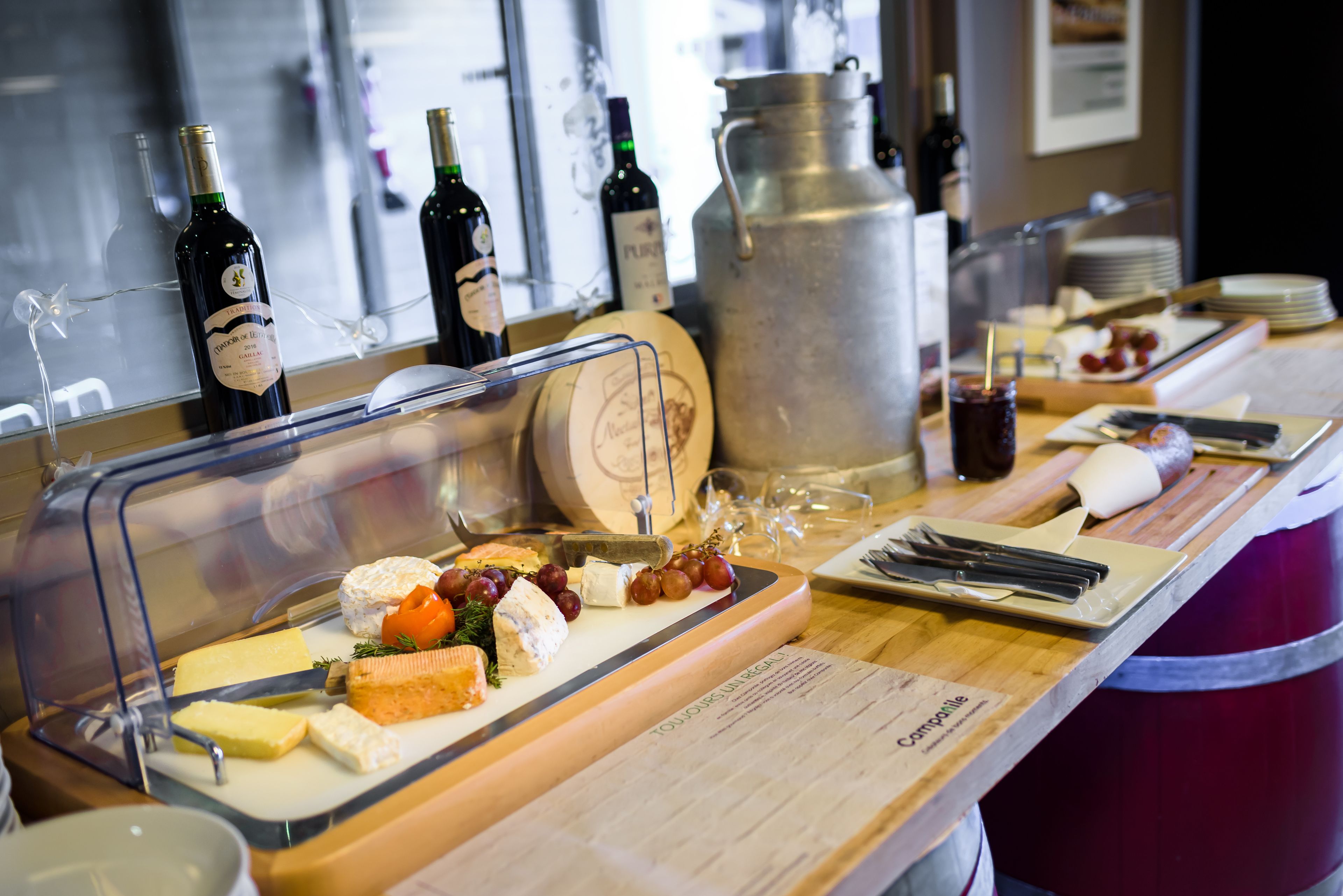 A buffet table with various cheeses, fruits, and wine bottles.