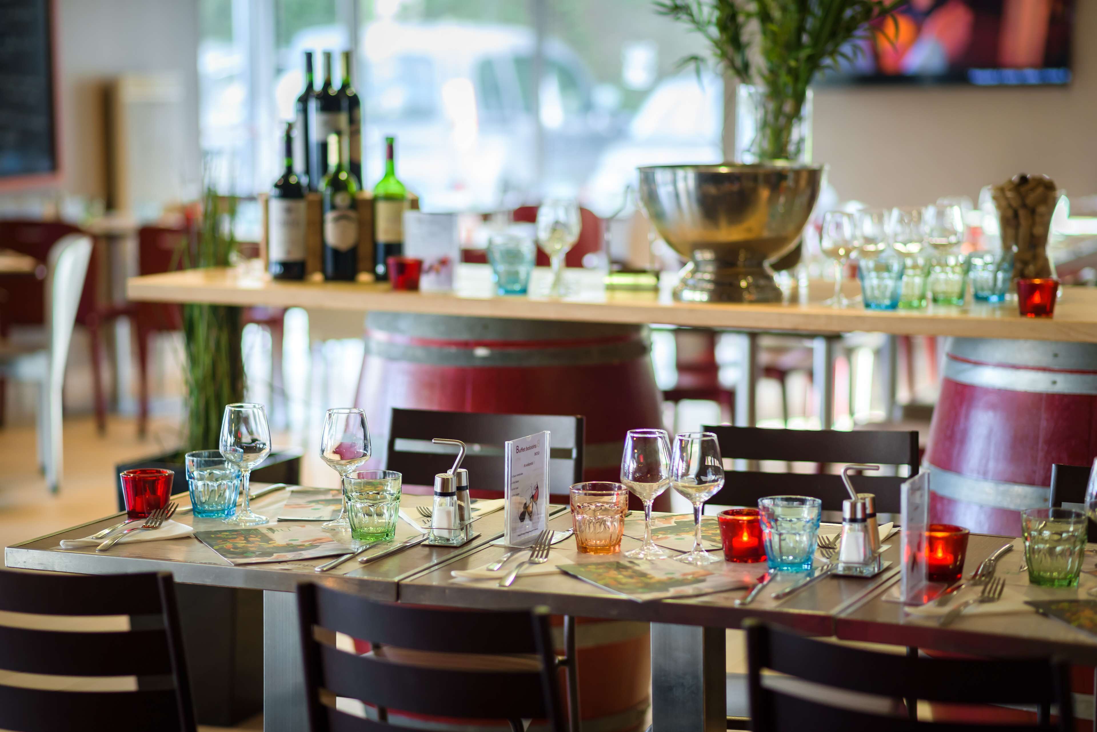Een restaurantscène met gedekte tafels, met wijnkleden, flessen en een grote metalen schaal op tafel.