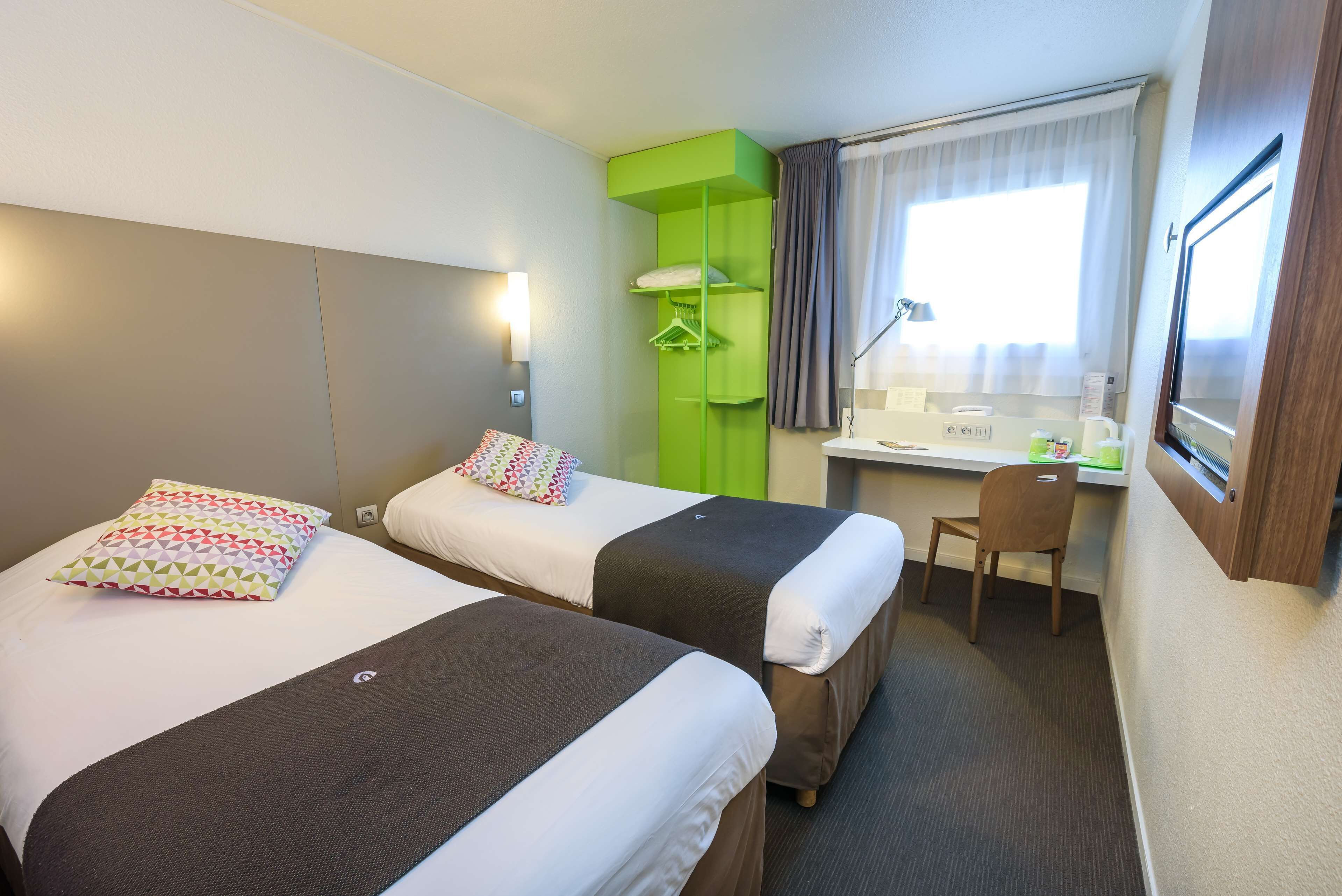 Ein Hotelzimmer mit zwei Betten, einem Schreibtisch, einem Stuhl und einem Fenster mit Vorhängen.