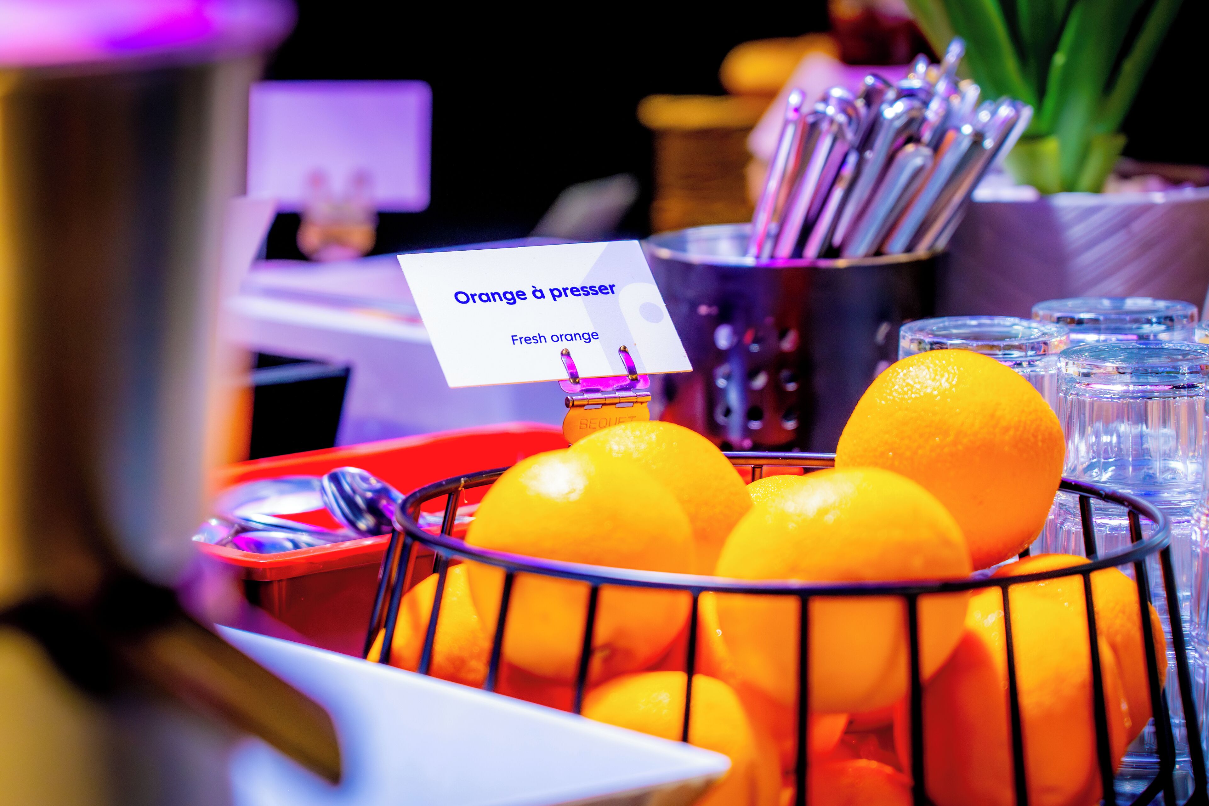 A basket of fresh oranges with a sign reading "Orange à presser" and a bottle of orange juice.