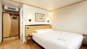 A hotel room with a wooden floor, a bed with white bedding, a nightstand, a wardrobe, and two wall-mounted lamps.