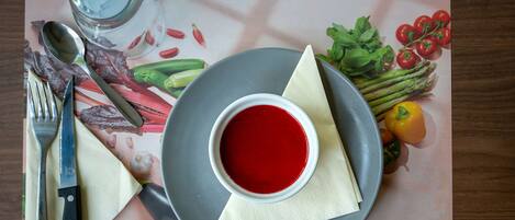 Una mesa servida con un tazón de sopa roja, un vaso de agua, un cuchillo, un tenedor, una cuchara y diversos vegetales.