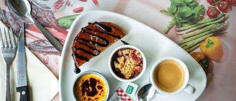 Un plato con postre, un bol de comida desmenuzada y una taza de café, junto con algunas verduras y una cuchara.