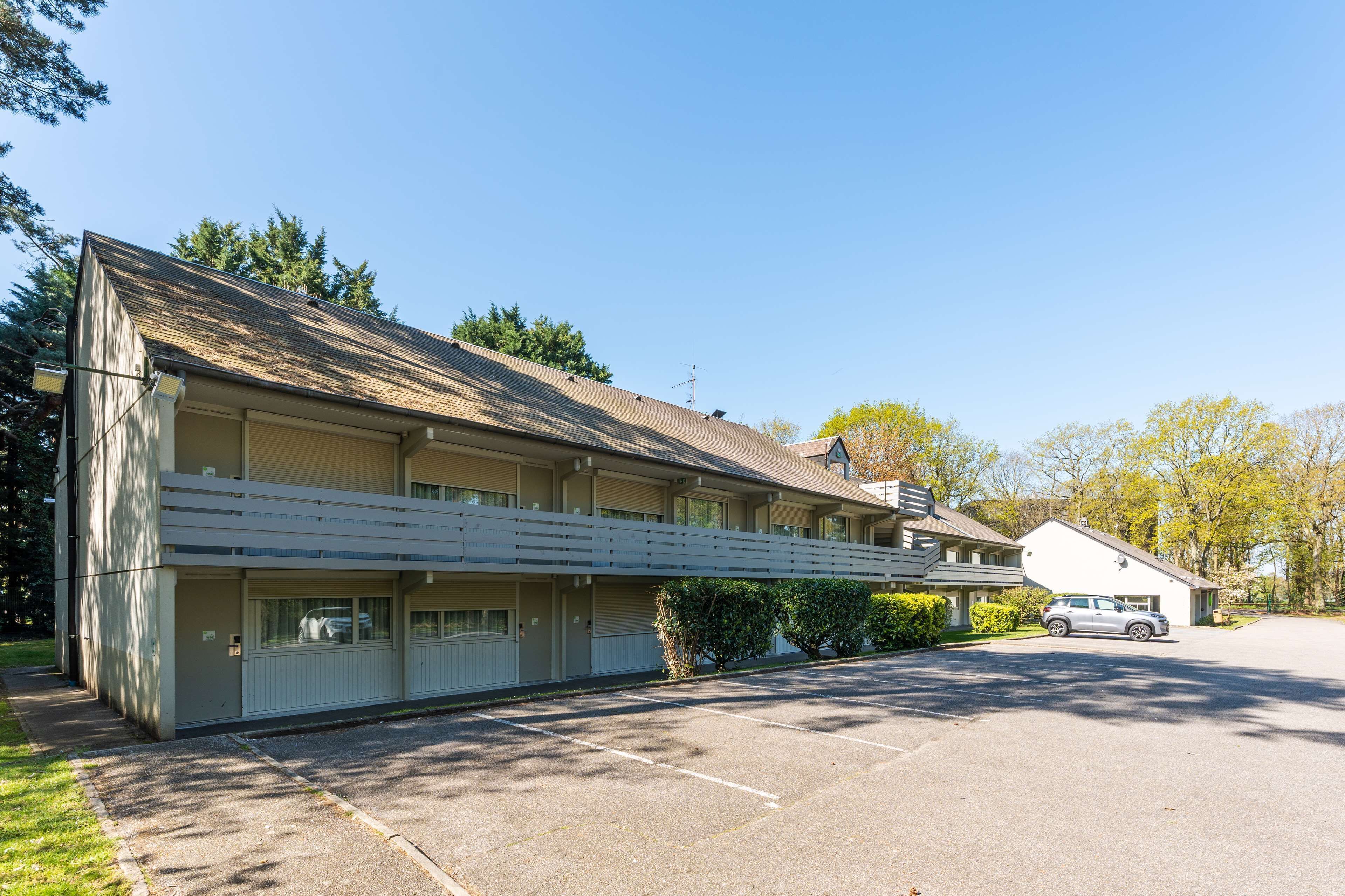 Un motel doté d’un parking couvert, d’une construction à un seul étage et d’un petit bâtiment attenant.