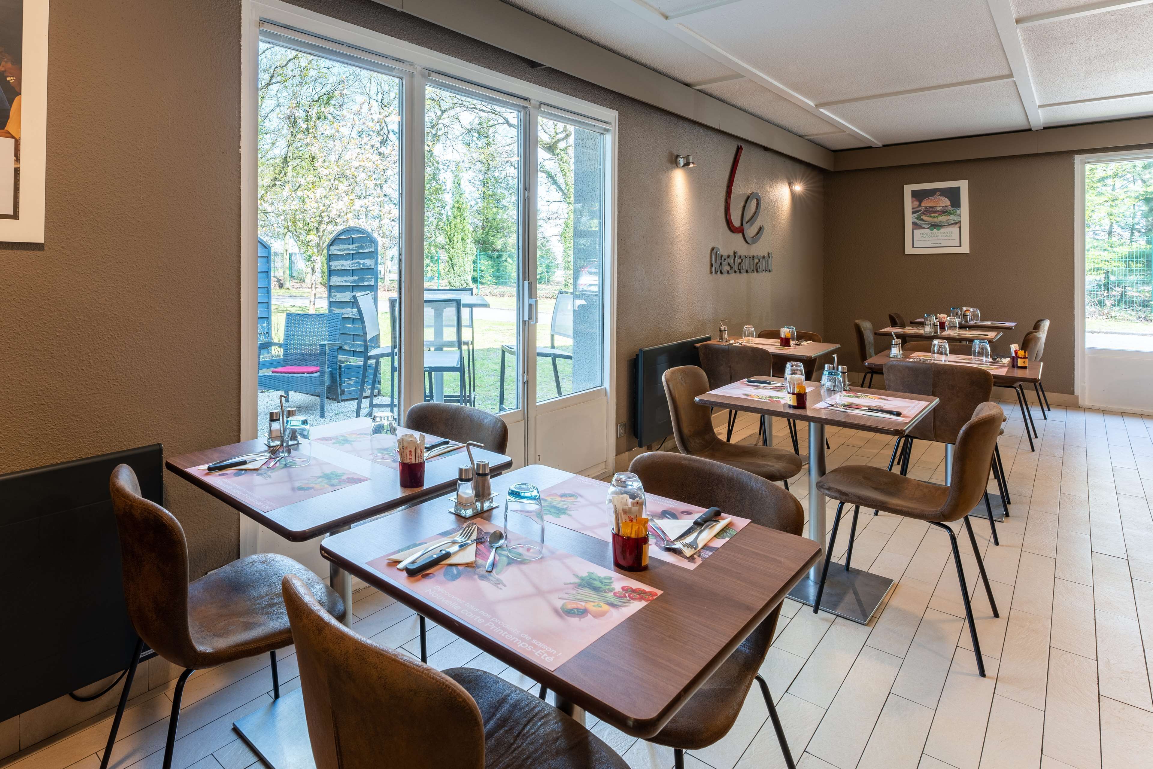 An indoor restaurant with tables set for dining, large windows, and a view of the outdoors.