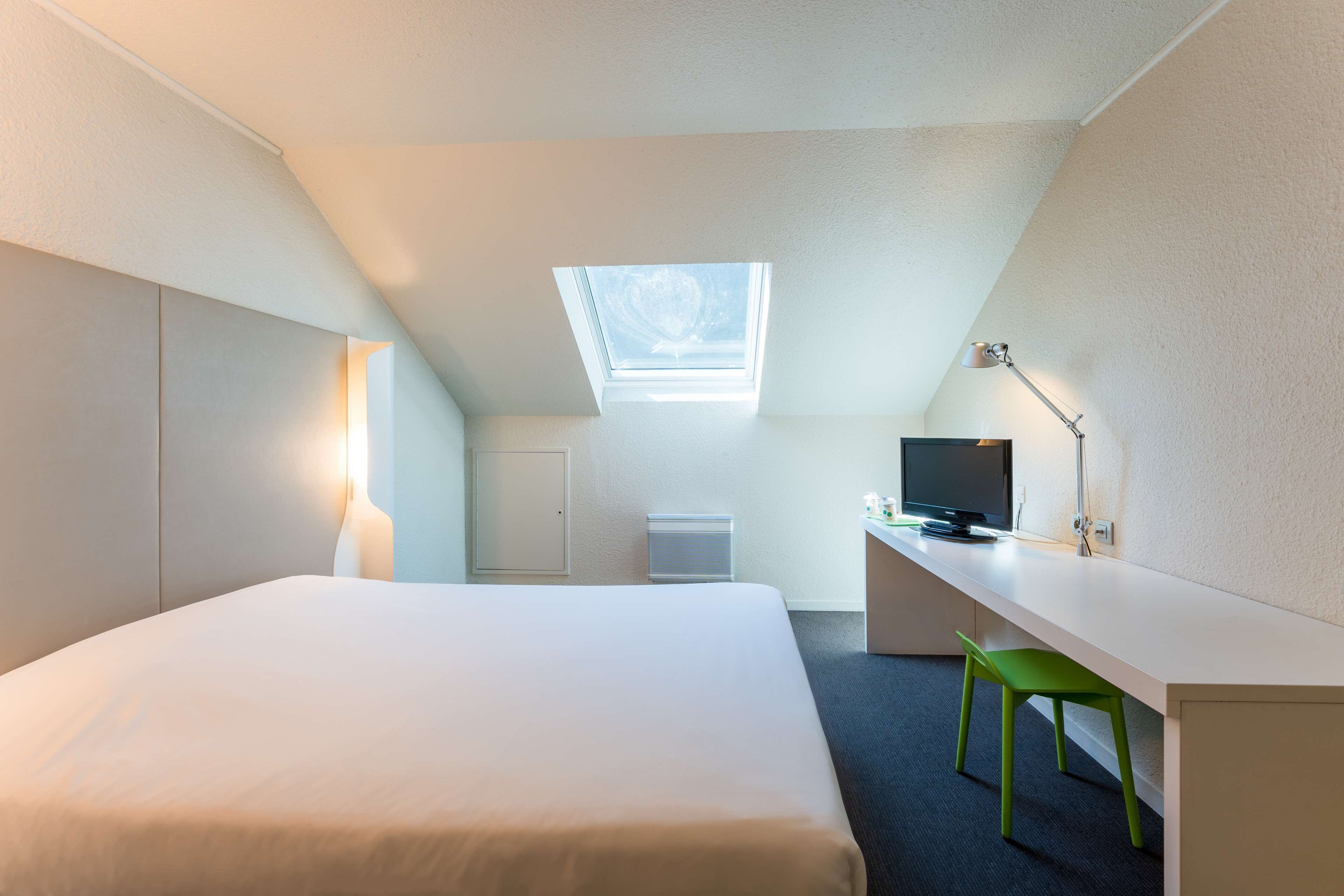 Una habitación de hotel moderna con cama, escritorio, silla, televisión y tragaluz.