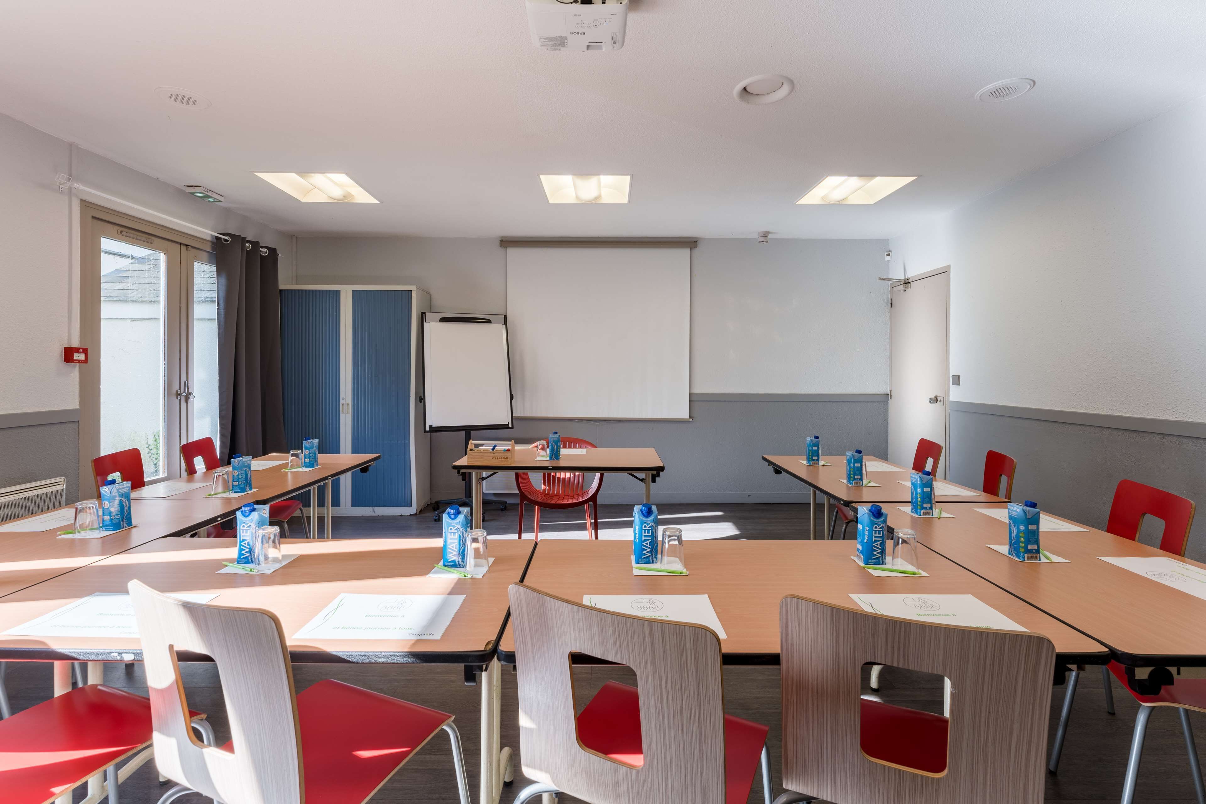 A conference room with a whiteboard, projector screen, and tables with chairs.