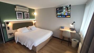 A hotel room with a bed, a desk, a chair, a TV, and a wall-mounted air conditioner.