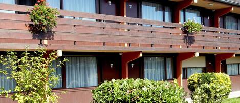 Un hotel con fachada roja, múltiples ventanas y balcones adornados con macetas de flores.