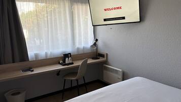 A hotel room with a bed, a desk with a chair, a TV displaying 'WELCOME', and a window with curtains.