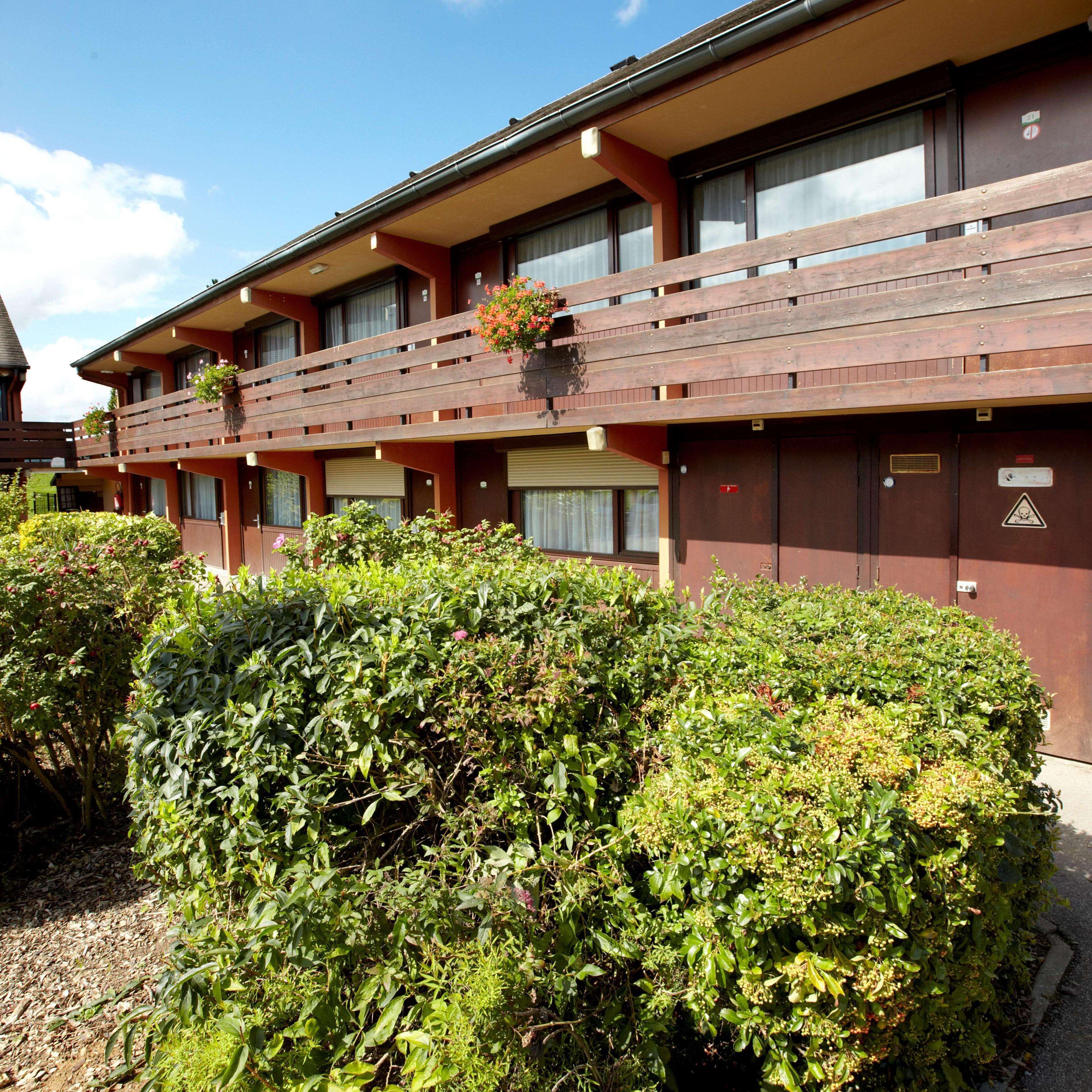 A multi-story building with balconies, a garden area, and a clear sky.