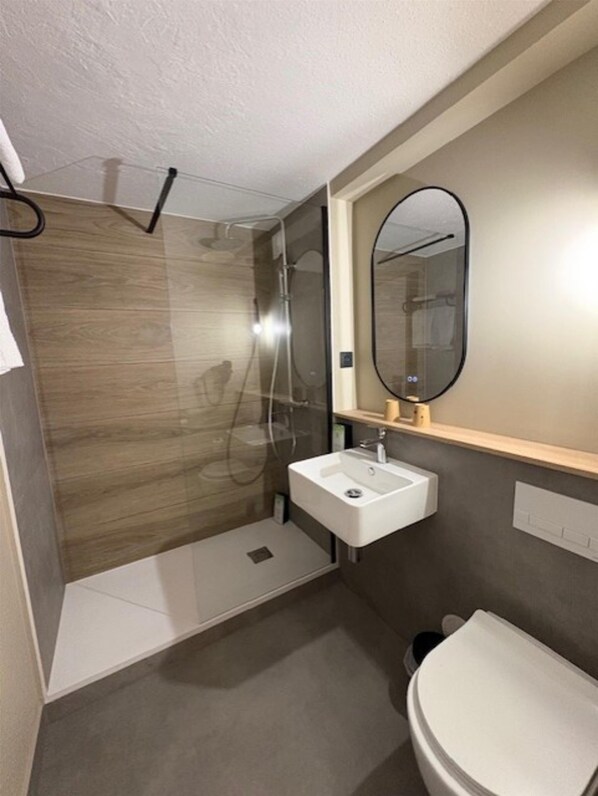 Un baño moderno con cabina de ducha de vidrio, un lavabo blanco y un inodoro.