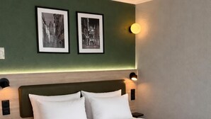 Een hotelkamer met een groot bed, twee aan de muur bevestigde fotolijstjes en bedlampjes.