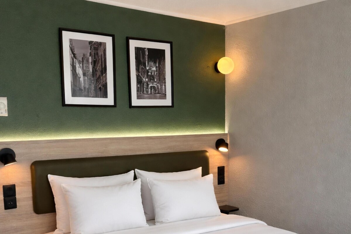 Une chambre d’hôtel avec un grand lit, deux cadres photos accrochés au mur et des lampes de chevet.
