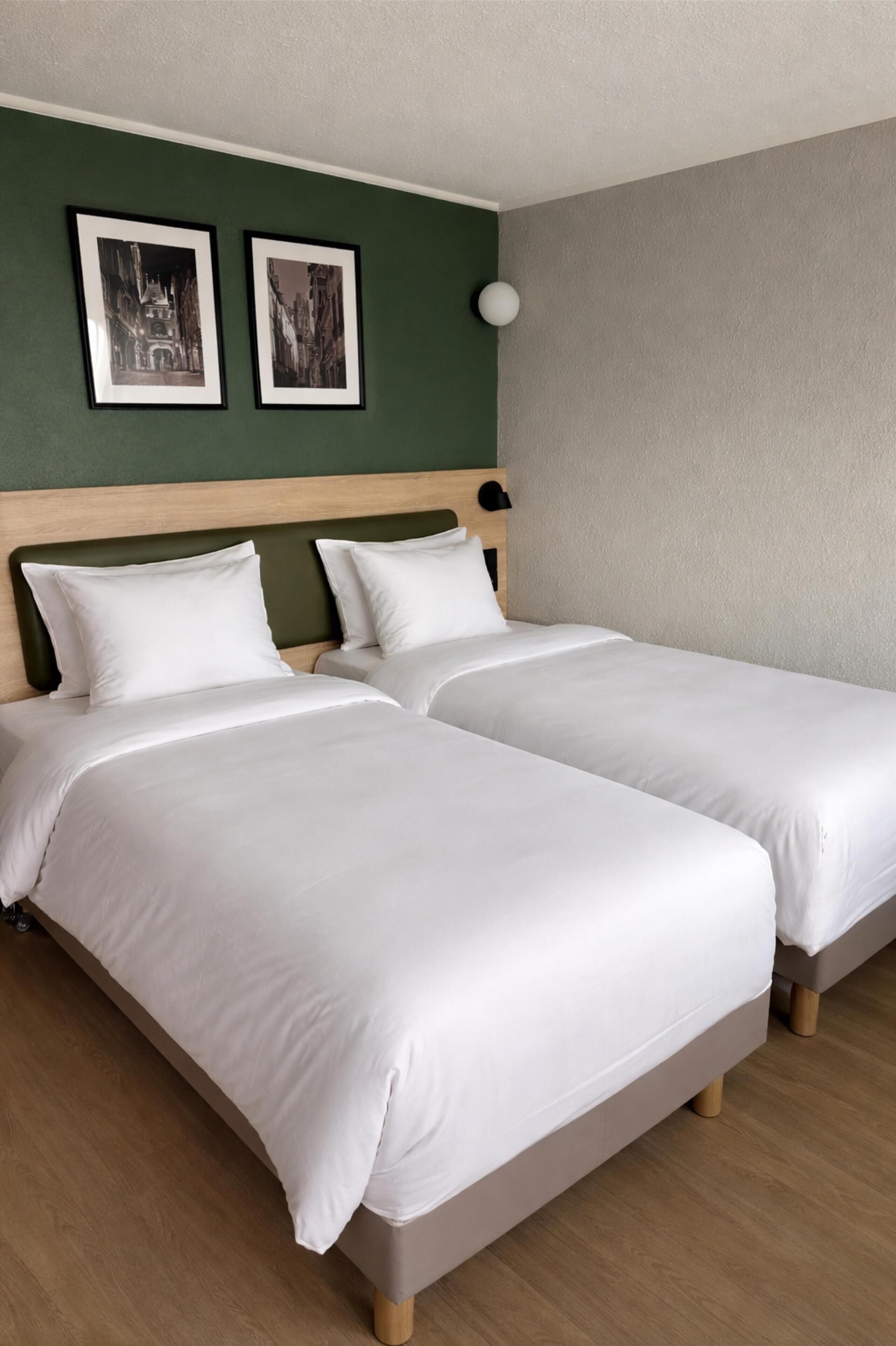 Un lit double avec du linge de lit blanc, une tête de lit en bois et deux tableaux encadrés accrochés au mur.